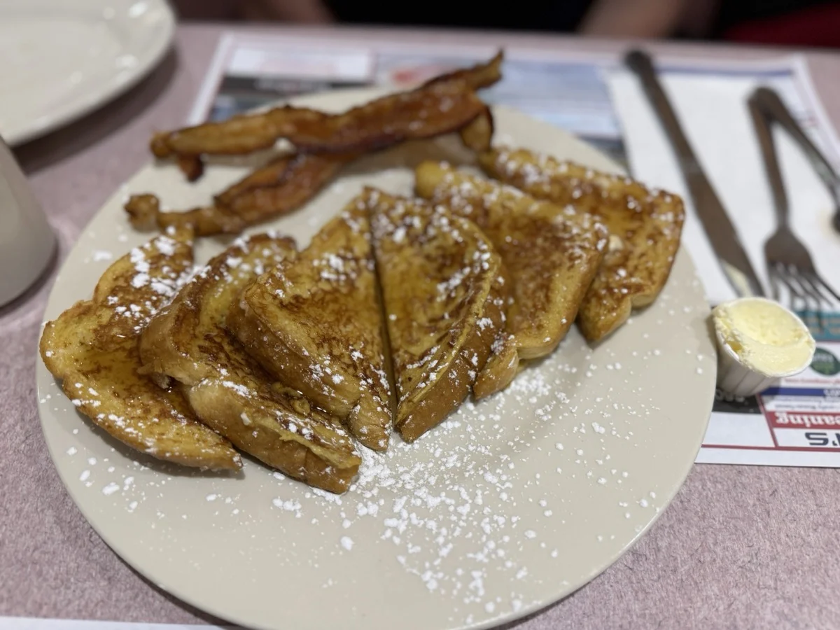 French toast dusted with powdered sugar, served with bacon.
